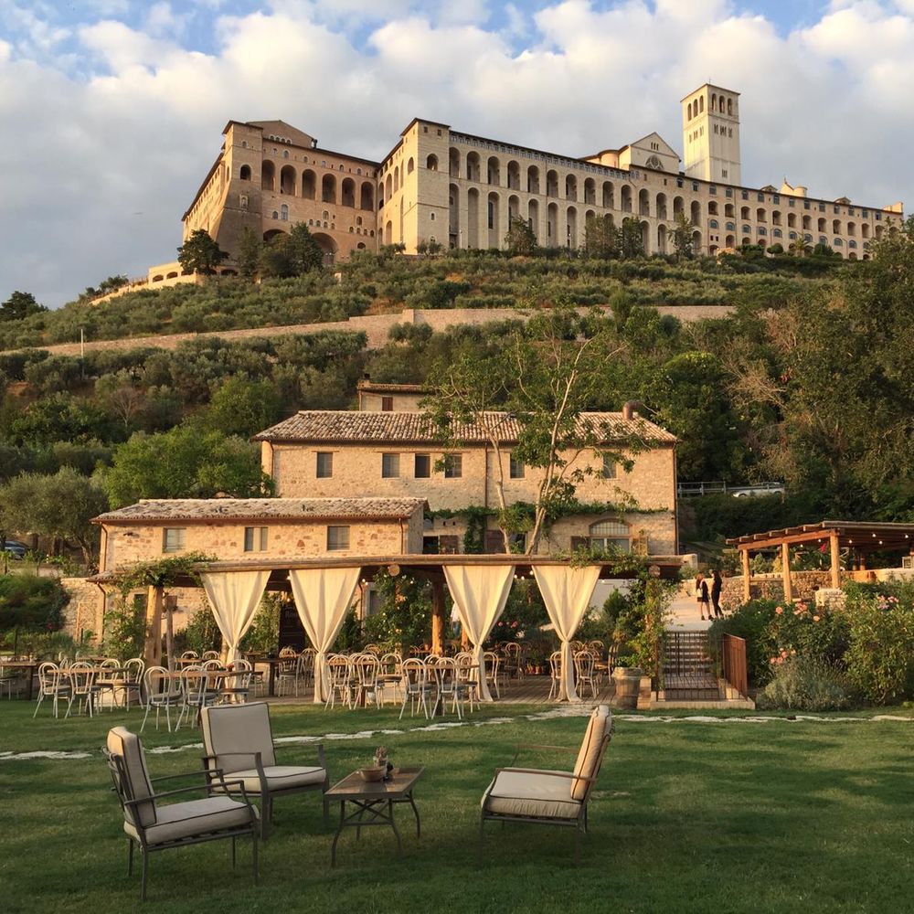 Outdoor Italian wedding reception with draped pergola and lawn seating below a hilltop stone town