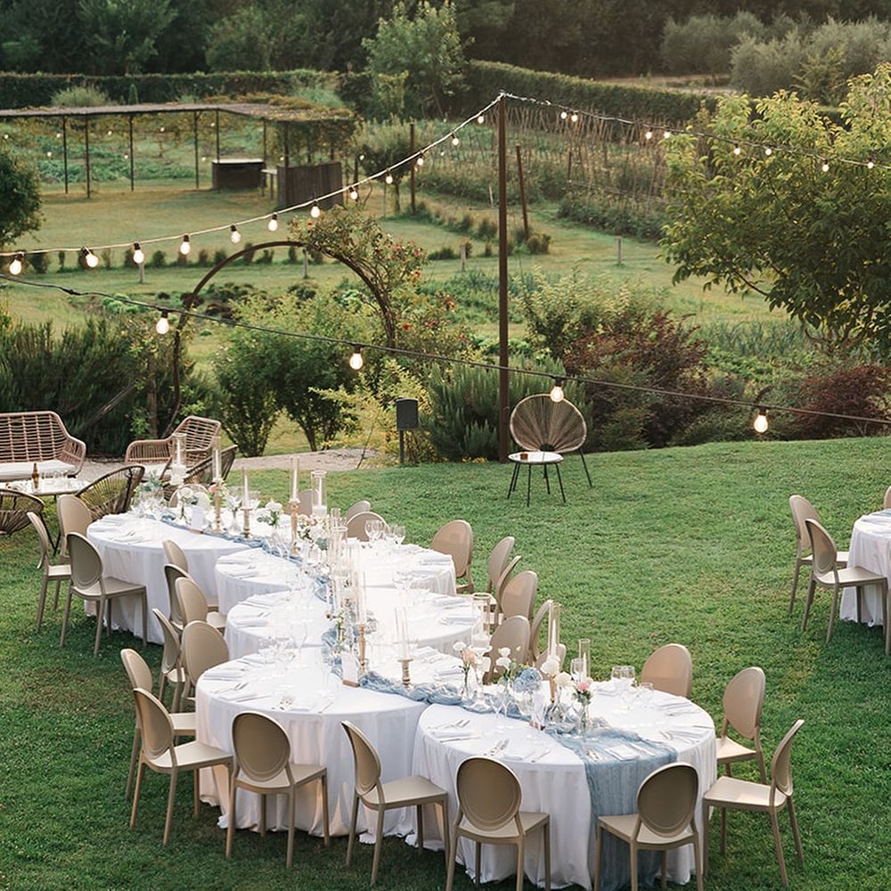 Outdoor wedding tables with dusty blue runners and festoon lights set on a garden lawn