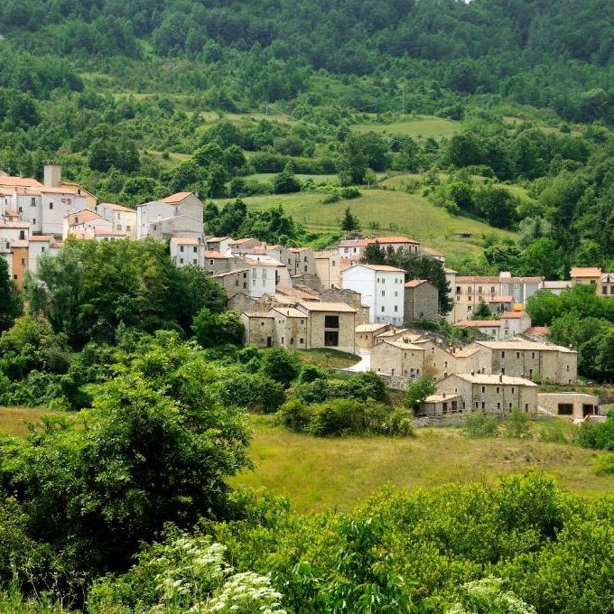 Hilltop stone village with a church tower nestled among lush green wooded hills and meadows