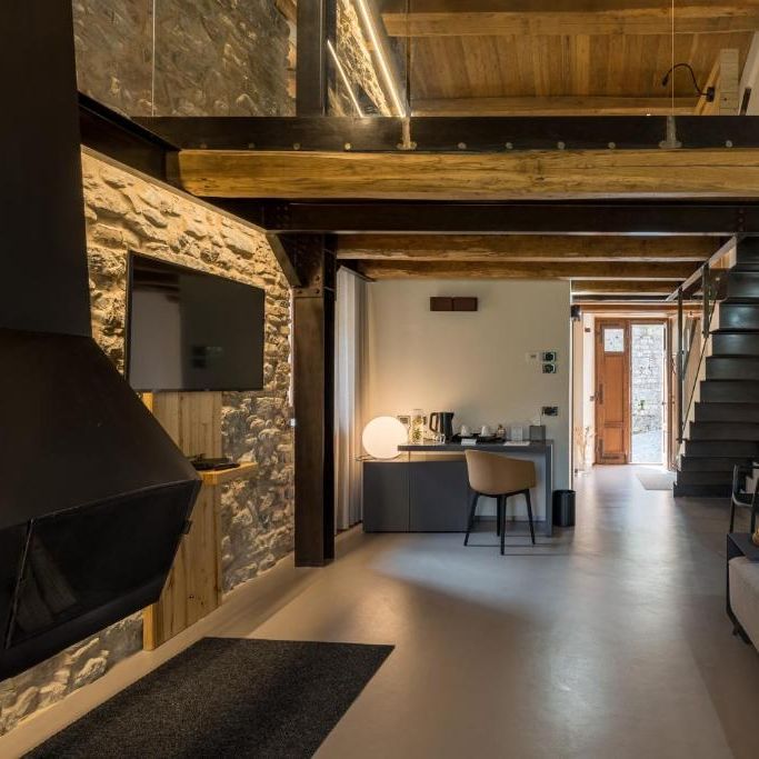 Modern rustic interior with exposed stone wall, timber beams and a floating staircase to a mezzanine.