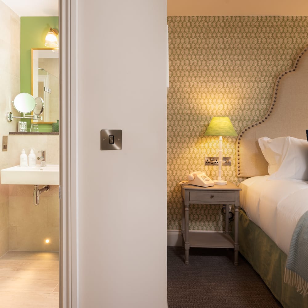 Boutique hotel bedroom with patterned headboard beside an ensuite shower room and basin.