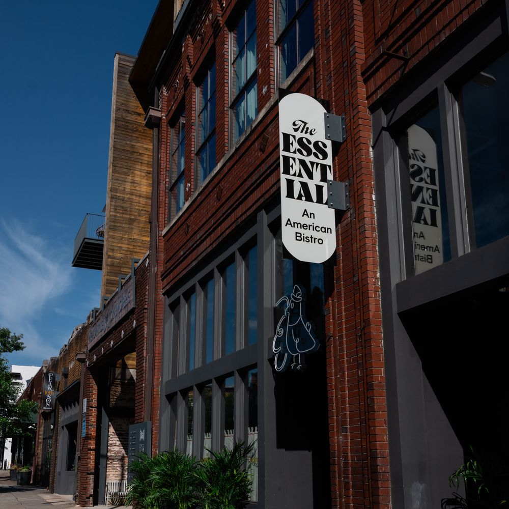 Brick bistro exterior with hanging sign and a floral-framed welcome sign on the pavement