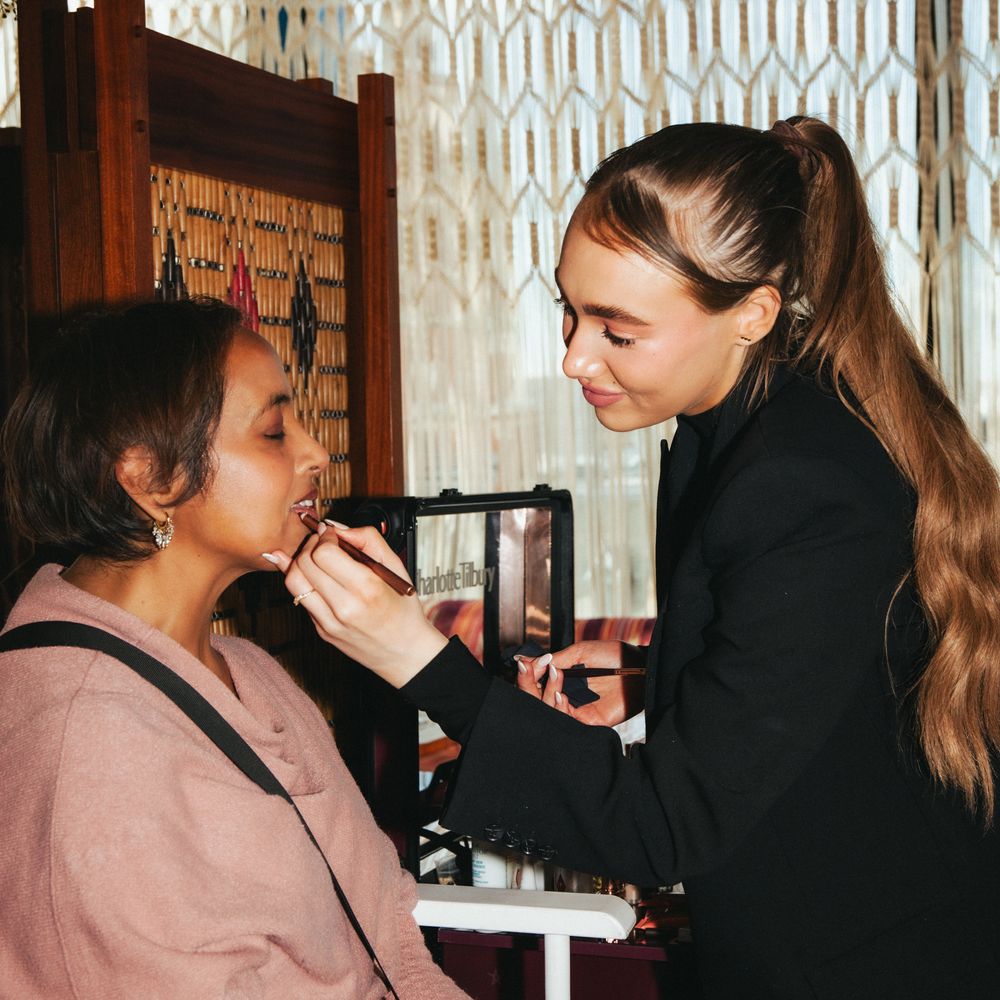 Makeup artist applying lipstick to a seated bride during morning bridal preparations