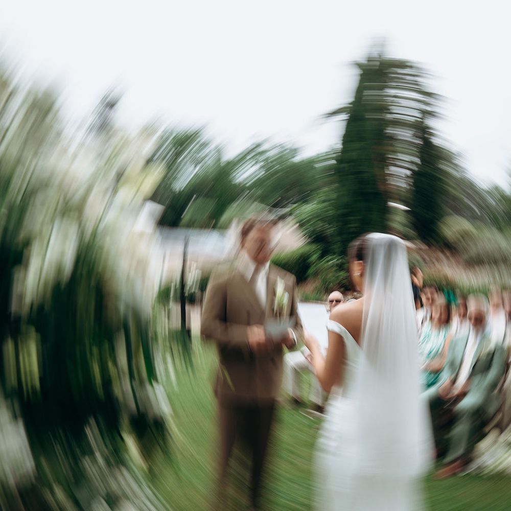 Bride in a long veil approaches the groom during an outdoor garden ceremony with motion blur