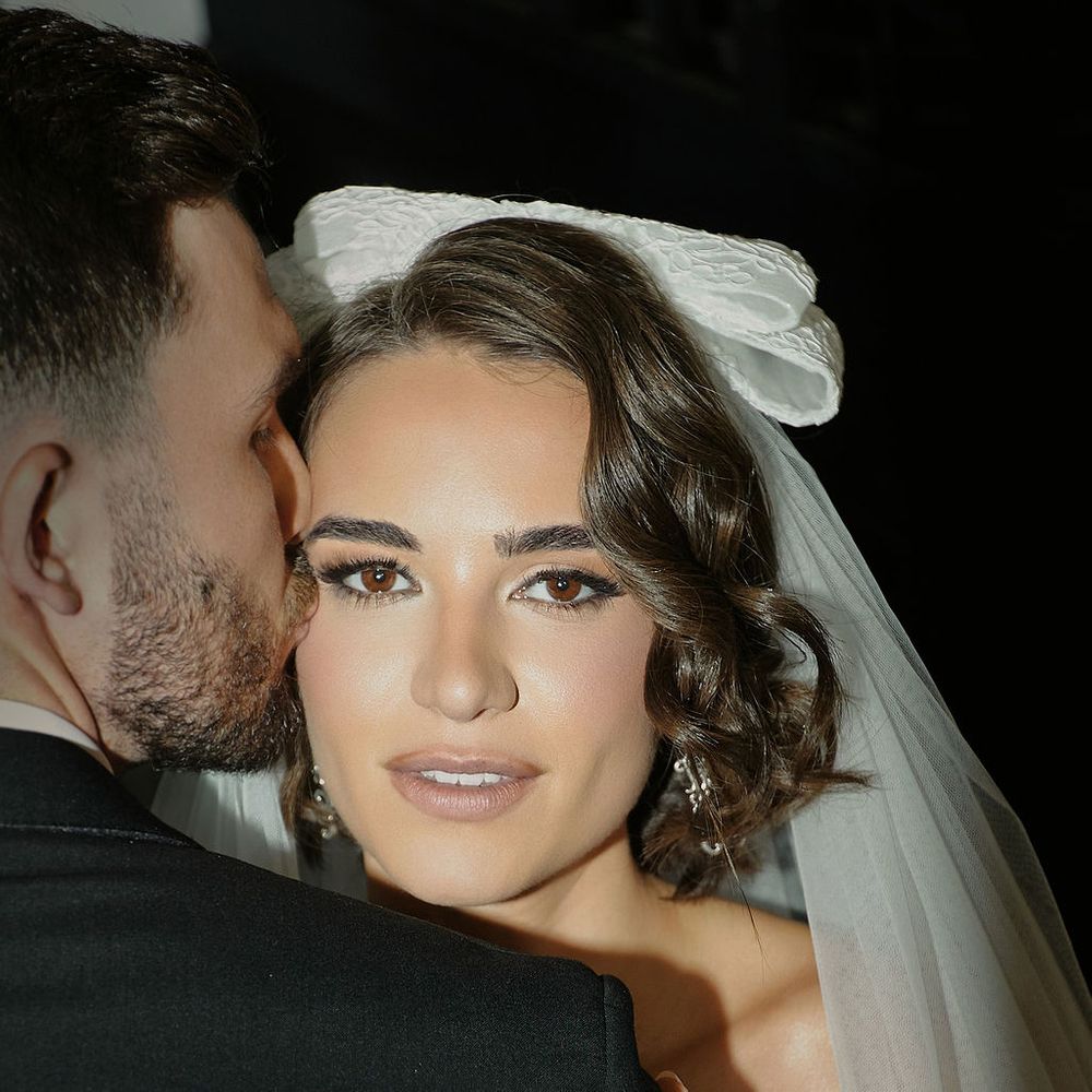 Groom kisses bride's cheek as she rests on his shoulder wearing a bow veil and diamond ring