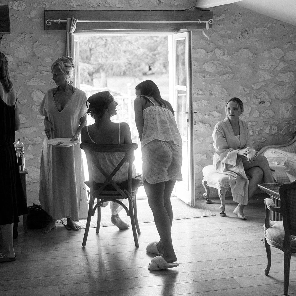 Bride and bridesmaids in loungewear preparing in a rustic stone room with exposed beams