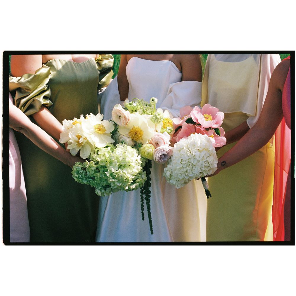 Bride and bridesmaids in pastel dresses holding peony and hydrangea bouquets outdoors