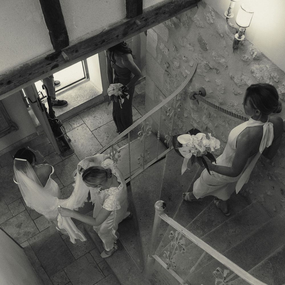 Bride descending a stone spiral staircase with bridesmaids carrying her veil and bouquets