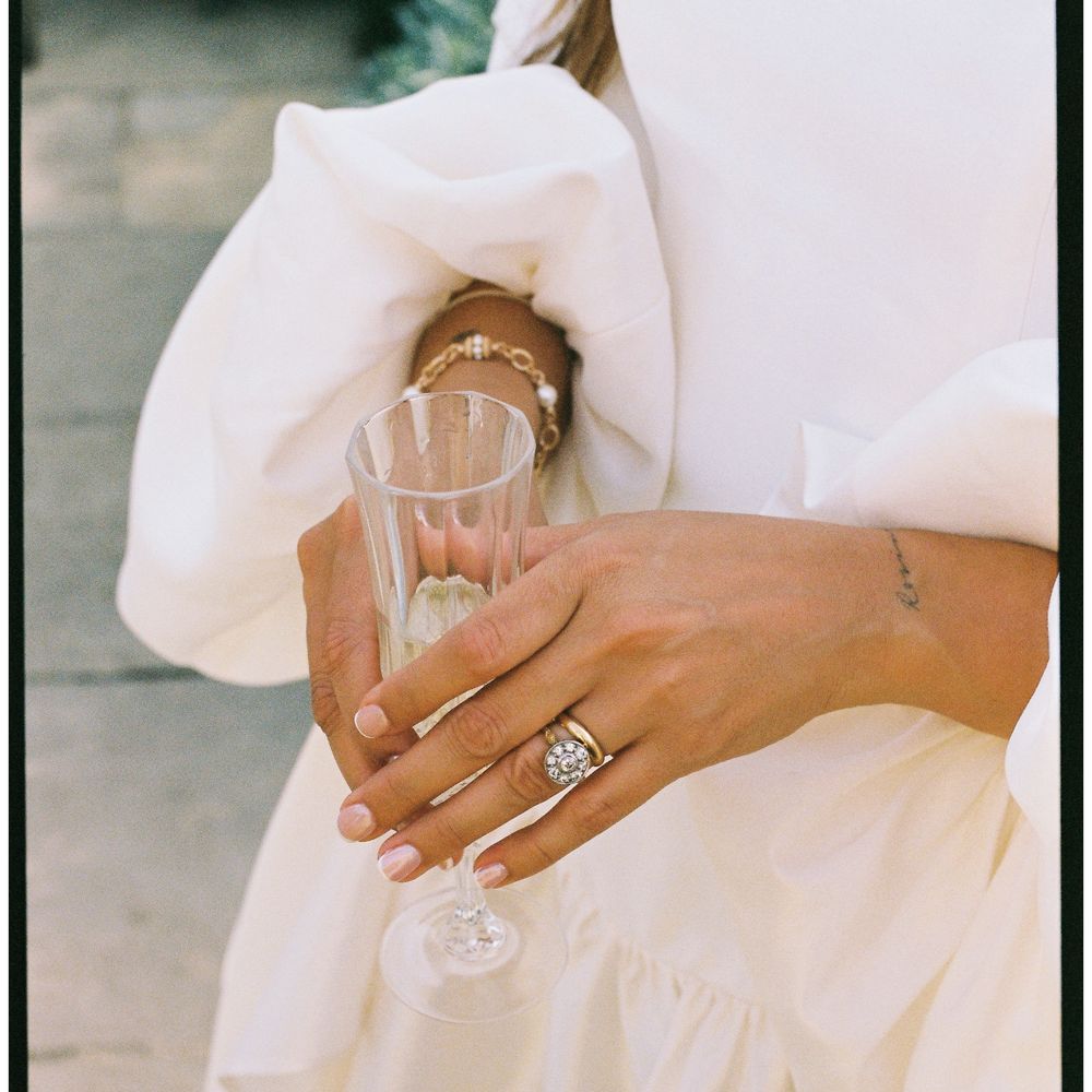 Bride in puff-sleeve gown holds a fluted champagne glass, showing her diamond ring and bracelet