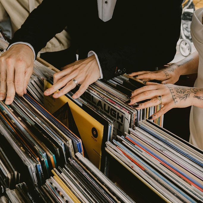 Bride and groom flick through vinyl records together, their wedding rings and tattoos visible