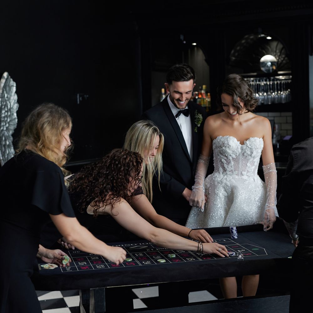 Bride and groom playing roulette with guests at a moody casino-themed reception bar