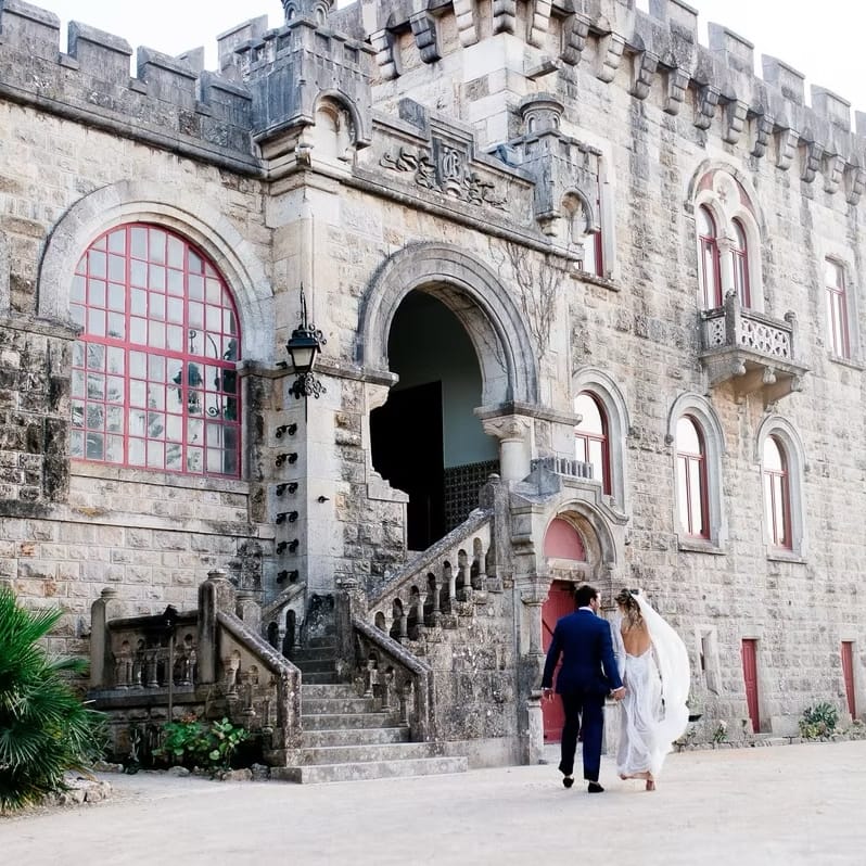 Bride and groom hand in hand walking towards the grand stone steps of a castle venue