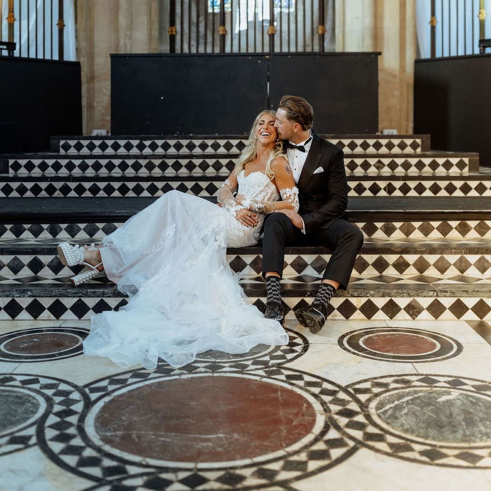Bride and groom sitting on chequered steps beneath stained glass windows in a Gothic cathedral