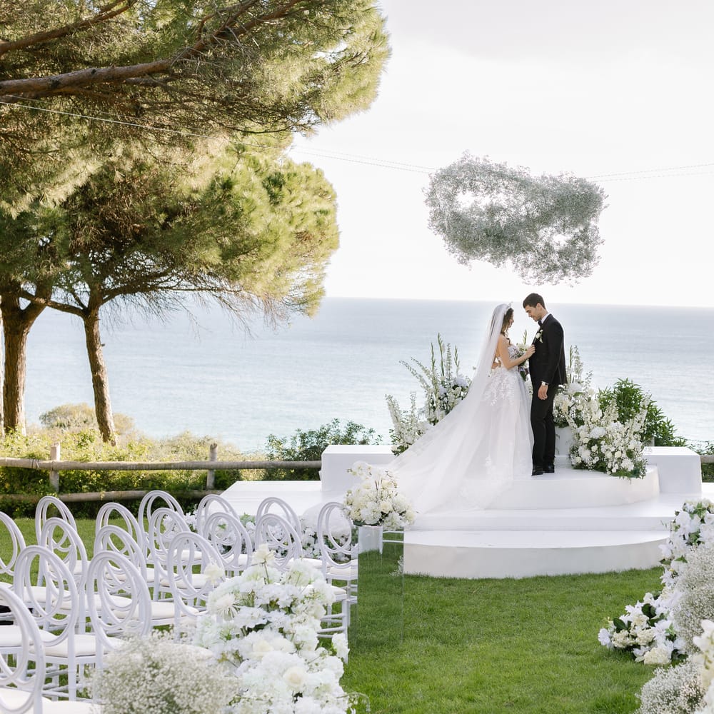 Bride and groom at a clifftop ceremony altar with white florals overlooking the sea