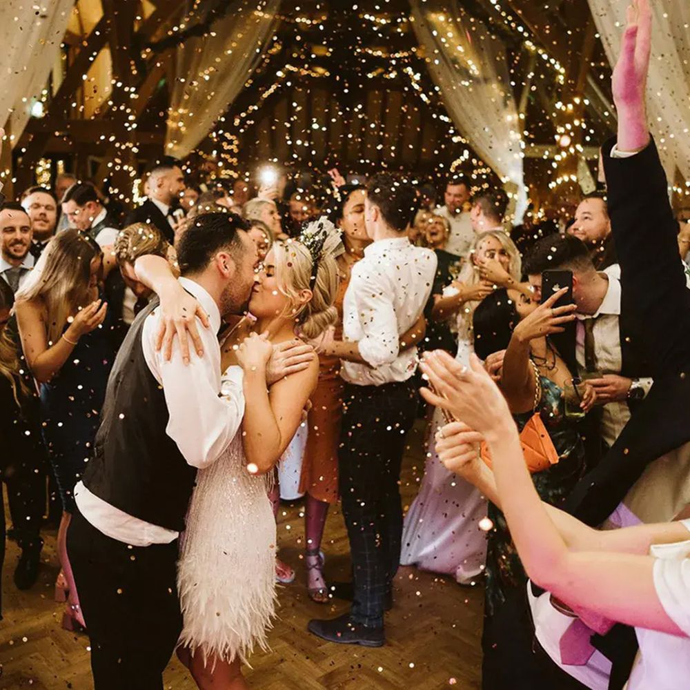 Bride and groom kiss on the dance floor as guests cheer amid falling confetti