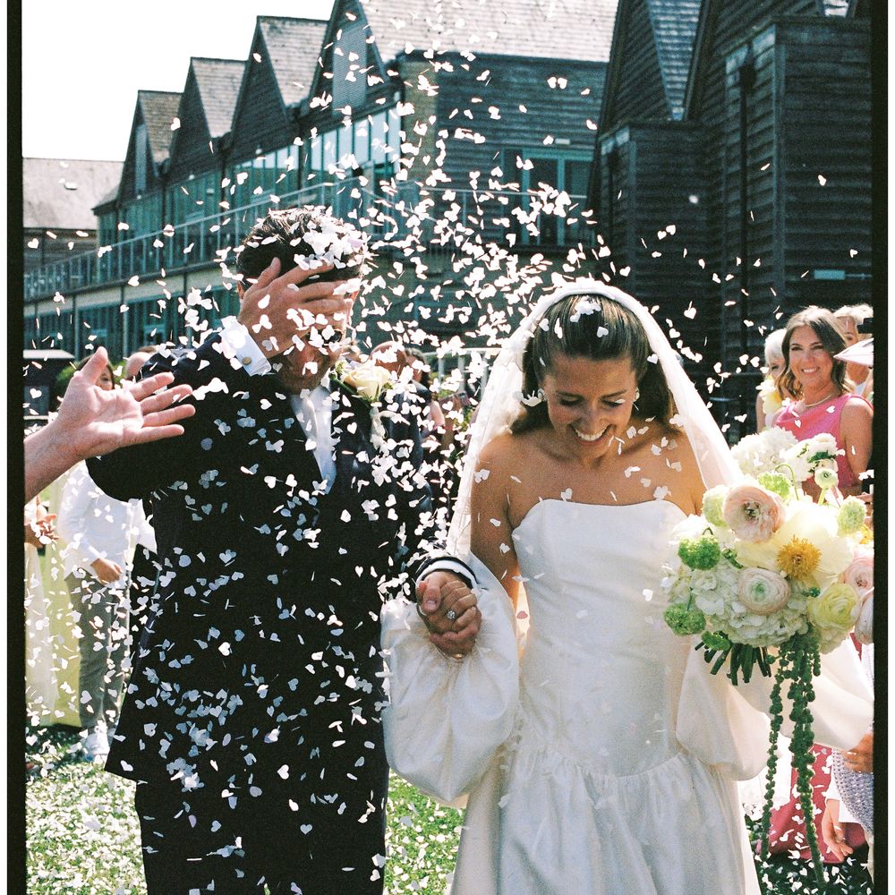 Bride and groom showered with confetti by guests as they walk hand in hand outdoors