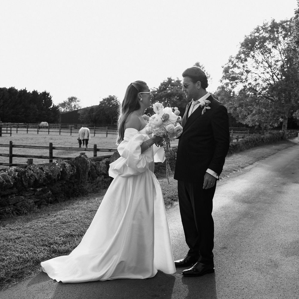 Bride and groom facing each other on a country lane beside a paddock in black and white