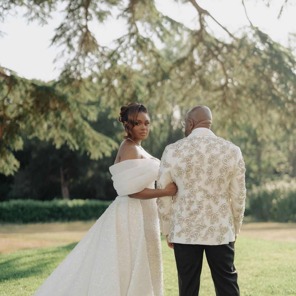 Bride in a sequinned off-shoulder gown and groom in an embellished ivory jacket on sunlit lawn