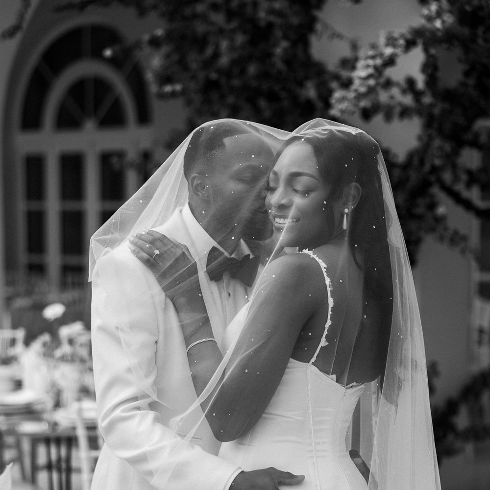 Bride and groom embracing beneath a pearl-embellished veil in a black and white portrait
