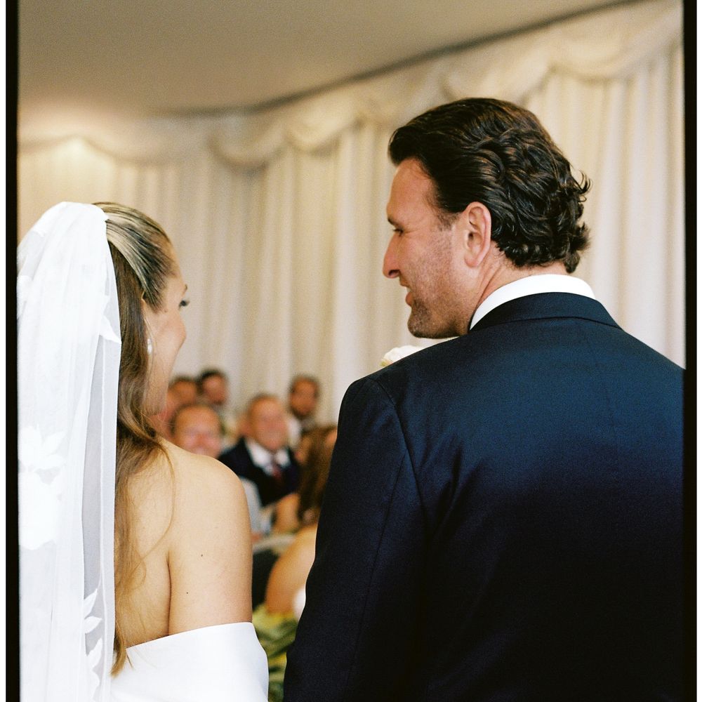 Bride and groom exchanging vows beneath white marquee drapes with guests looking on