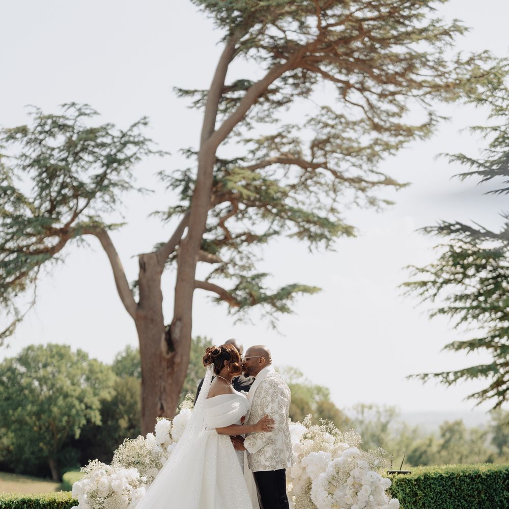 Bride and groom kiss on a white circular platform surrounded by white floral displays outdoors