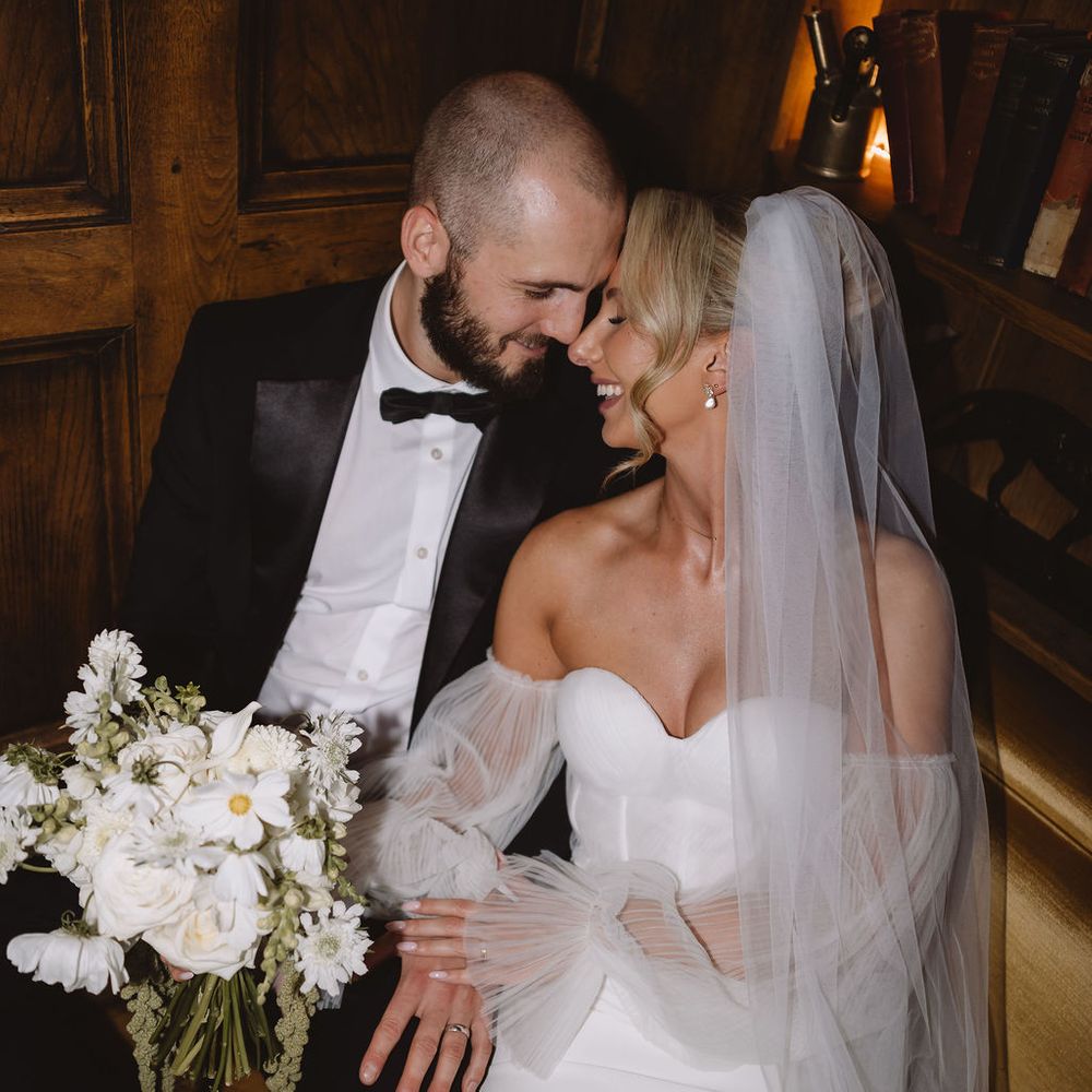 Bride and groom share an intimate moment against oak panelling with a white bouquet