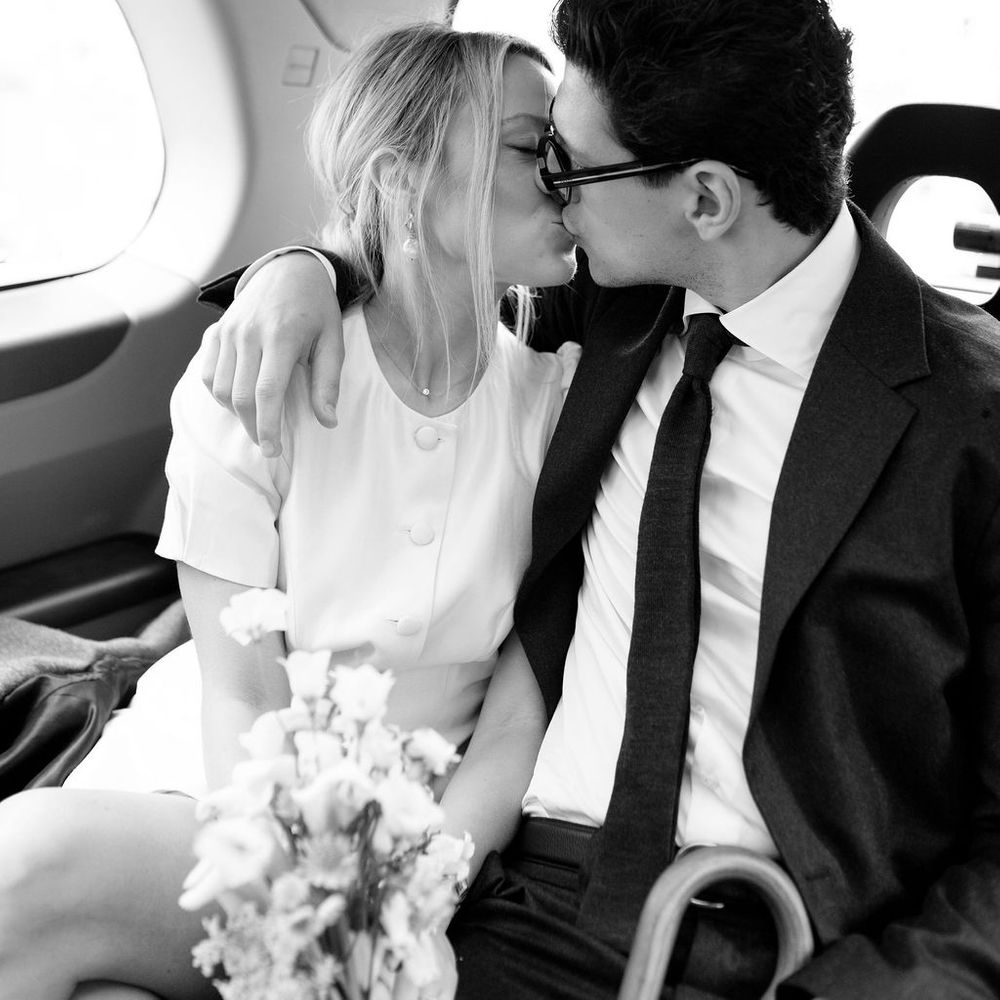 Black and white photo of a bride and groom sharing a kiss in the back of a car