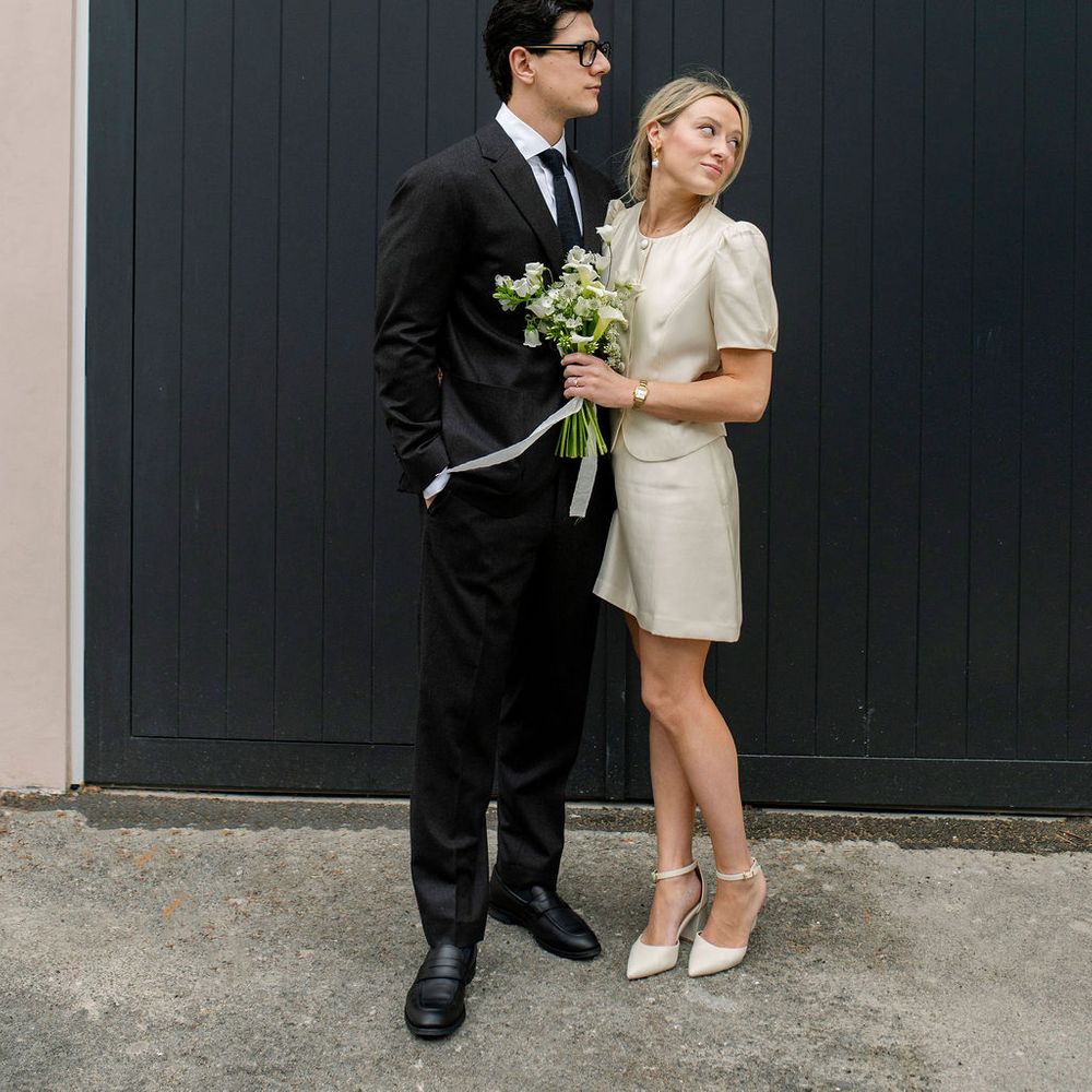 Bride in short cream dress and groom in dark suit stand by a navy garage door