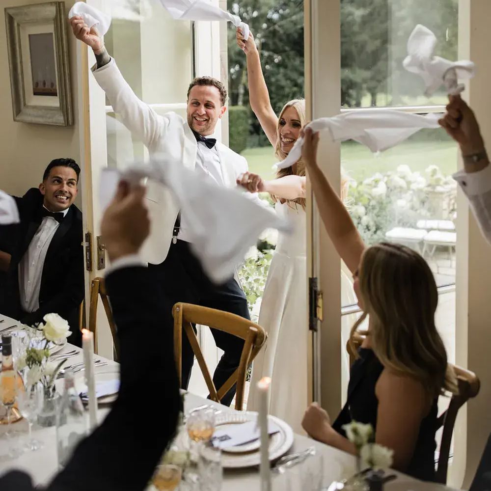 Bride and groom wave white napkins in the air as guests celebrate at their reception