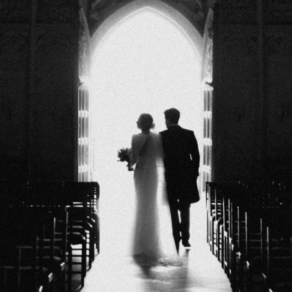Bride and groom silhouetted against a bright Gothic archway as they leave a chapel