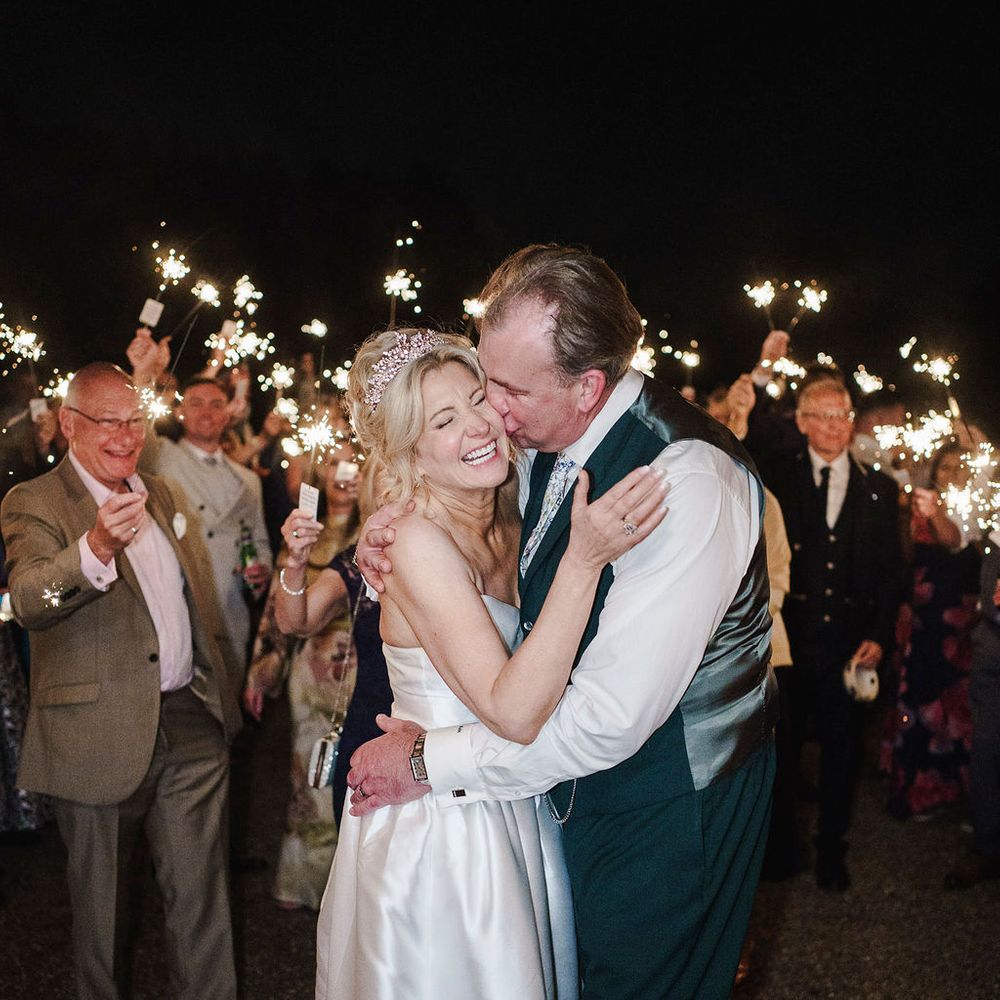 Bride and groom embrace as guests hold sparklers aloft during an evening celebration