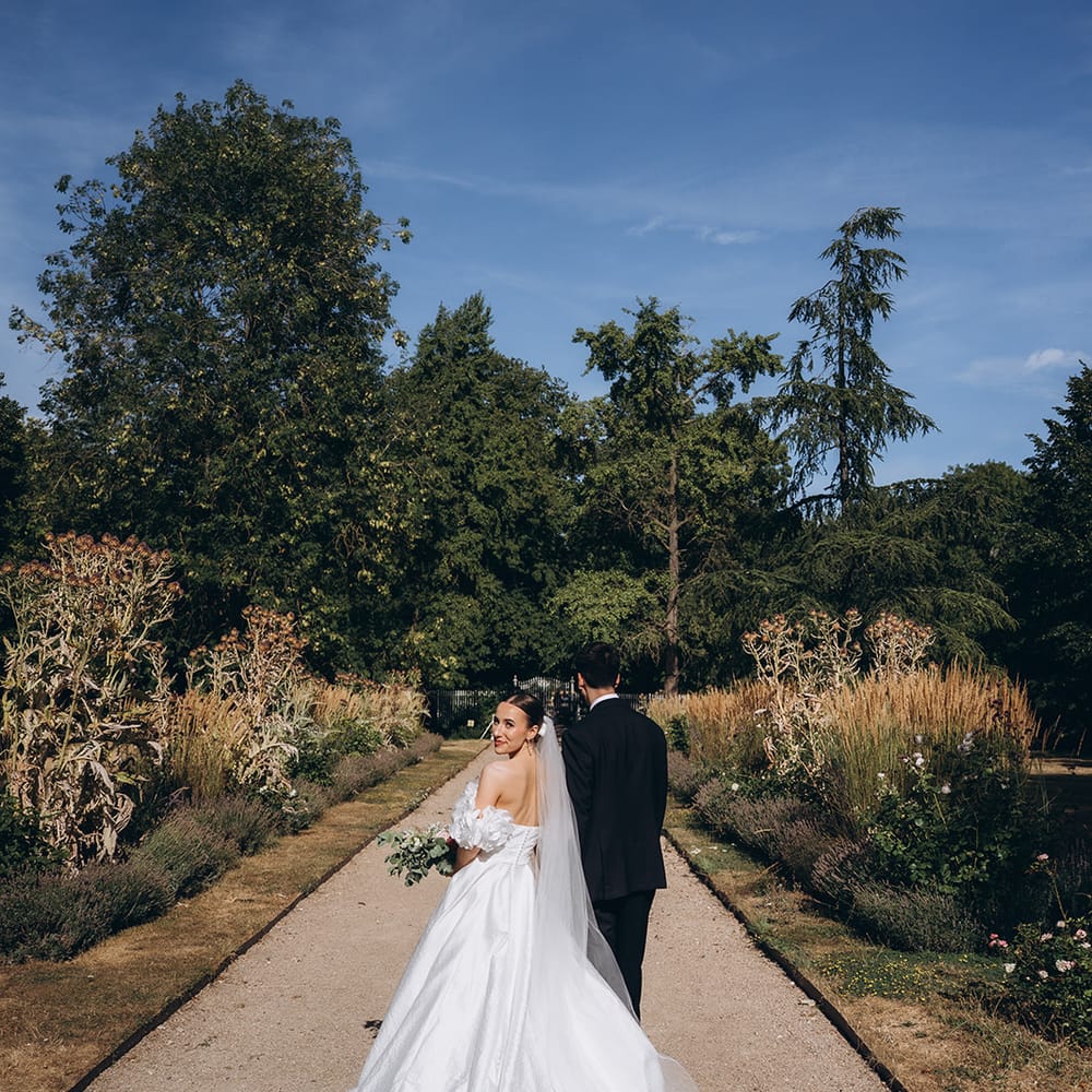 Bride glancing back over her shoulder as she walks a garden path with her groom