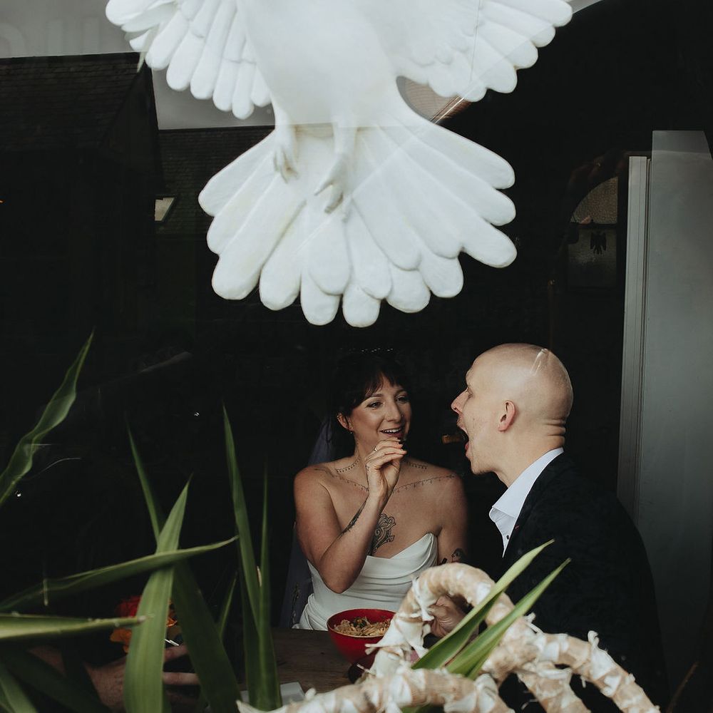 Bride and groom laughing together seen through a window with a large white dove decoration