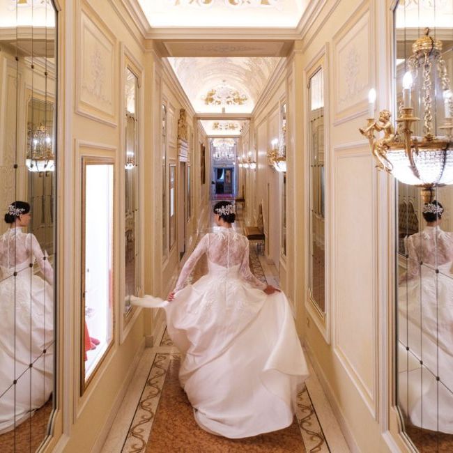 Bride in a lace-sleeved gown walking down a mirrored corridor with ornate gilt detailing