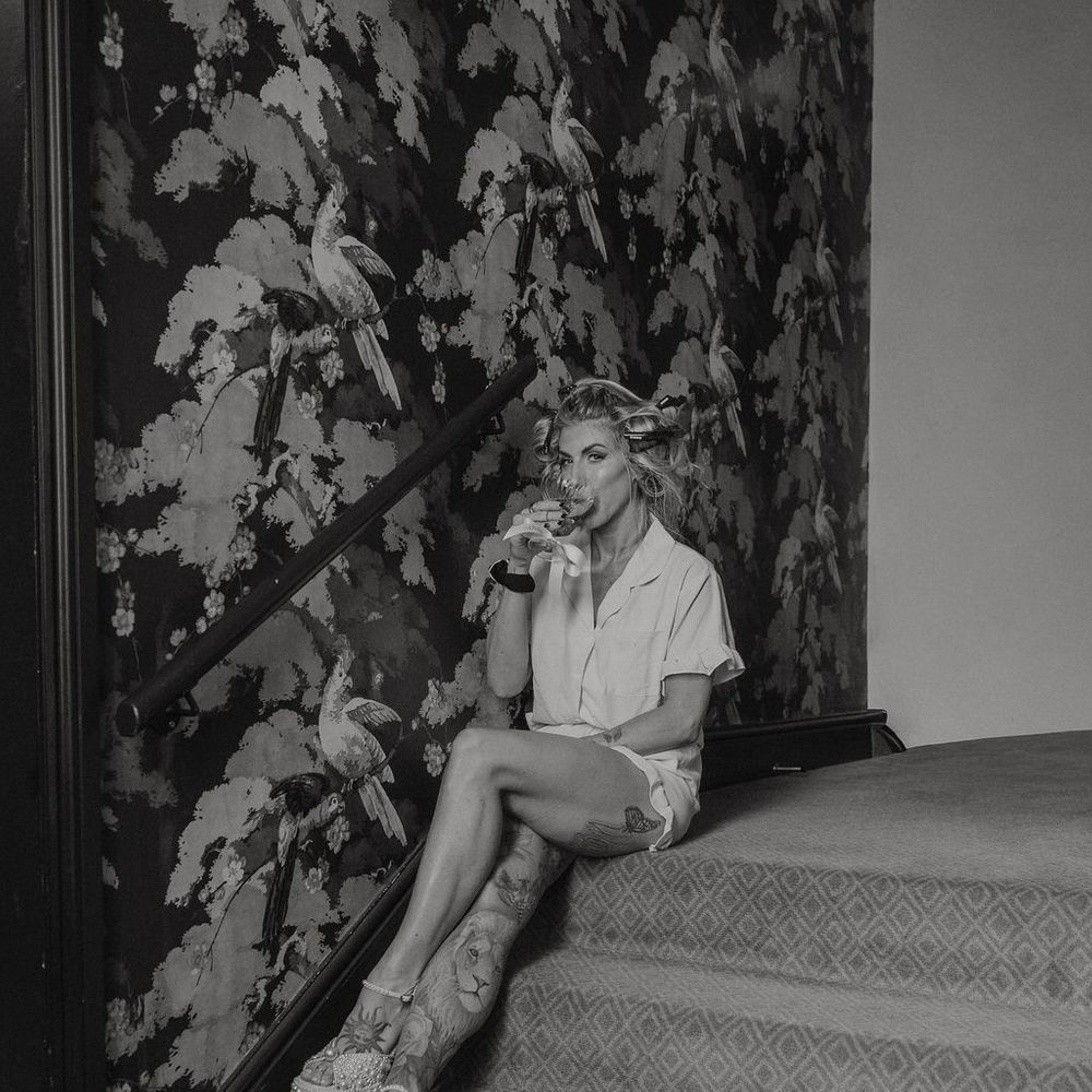 Bride in pyjamas and pearl heels sips a drink on patterned staircase during morning prep