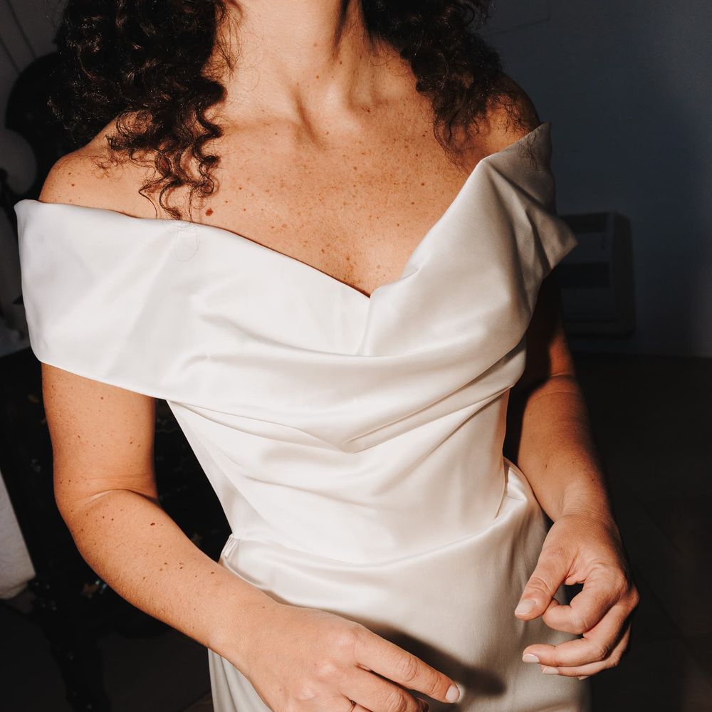 Bride in an off-the-shoulder satin gown with draped bardot neckline and delicate engagement ring