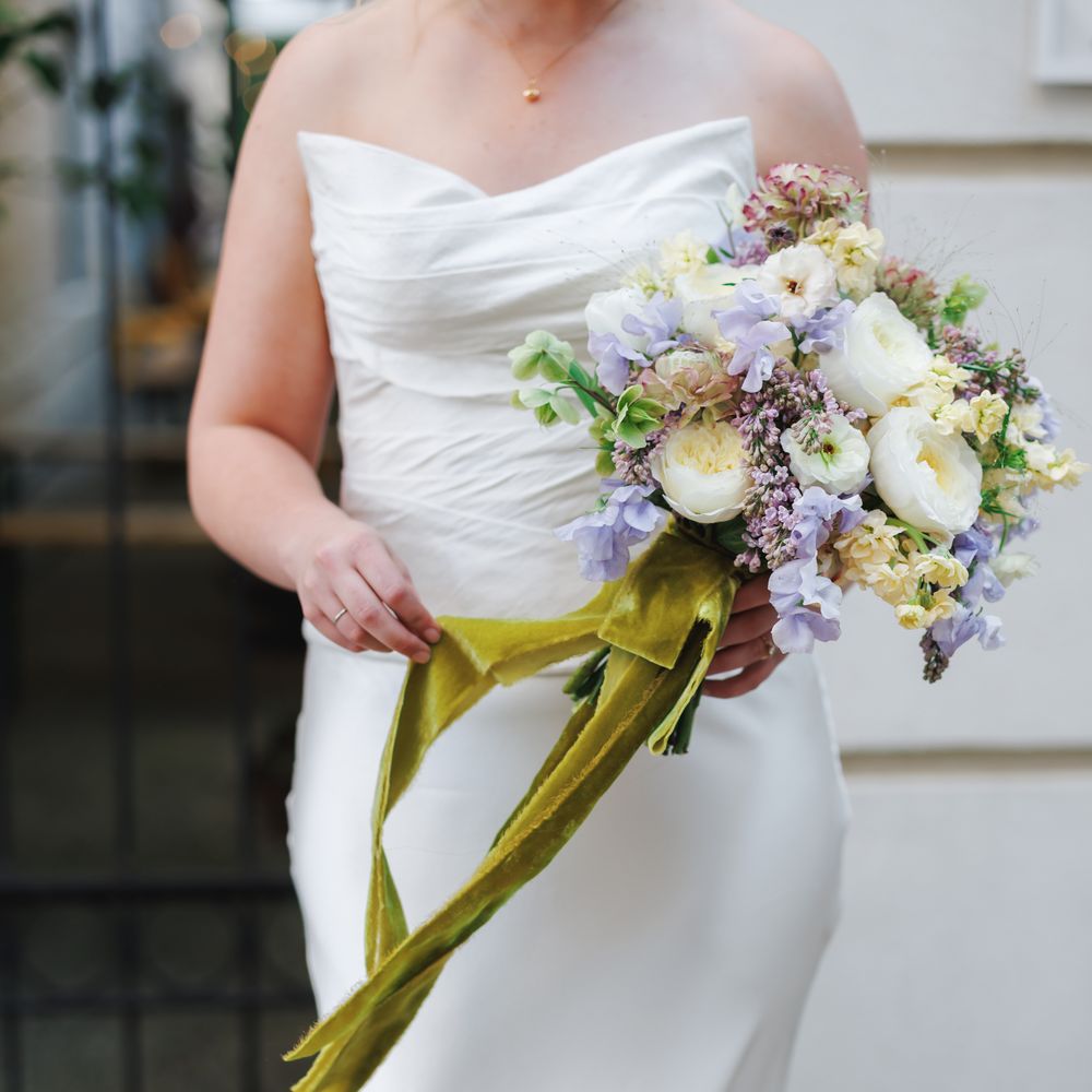 Bride in a strapless satin gown holding a pastel bouquet tied with green velvet ribbon