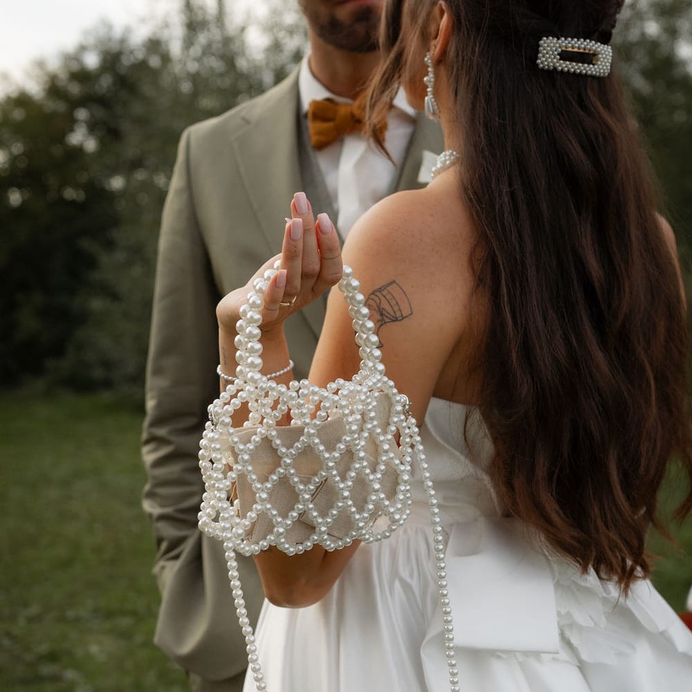 Bride holding a beaded pearl bag beside a groom in a sage suit and mustard bow tie