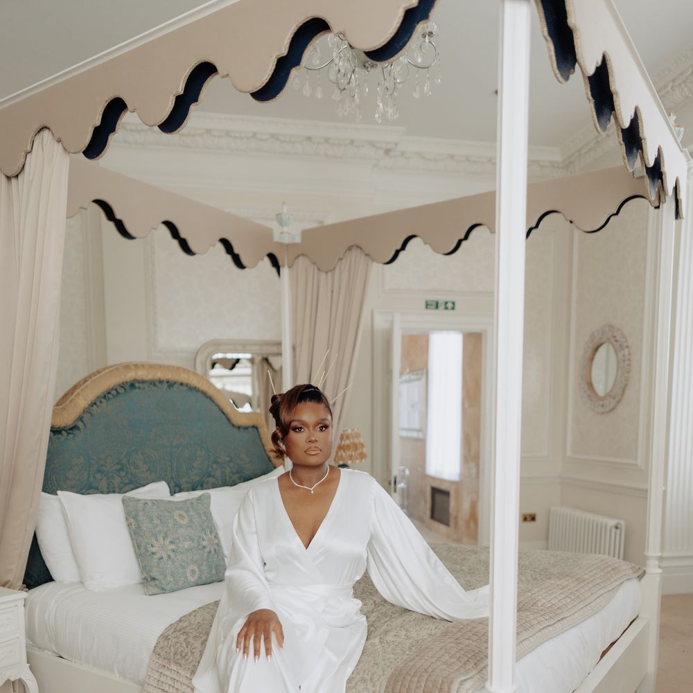 Bride in a satin wrap gown seated on a four-poster bed in an elegant bridal suite
