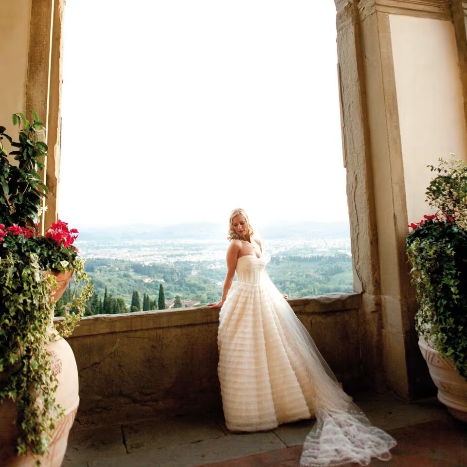 Bride in a full tulle ballgown stands beneath a stone archway overlooking a hilltop valley