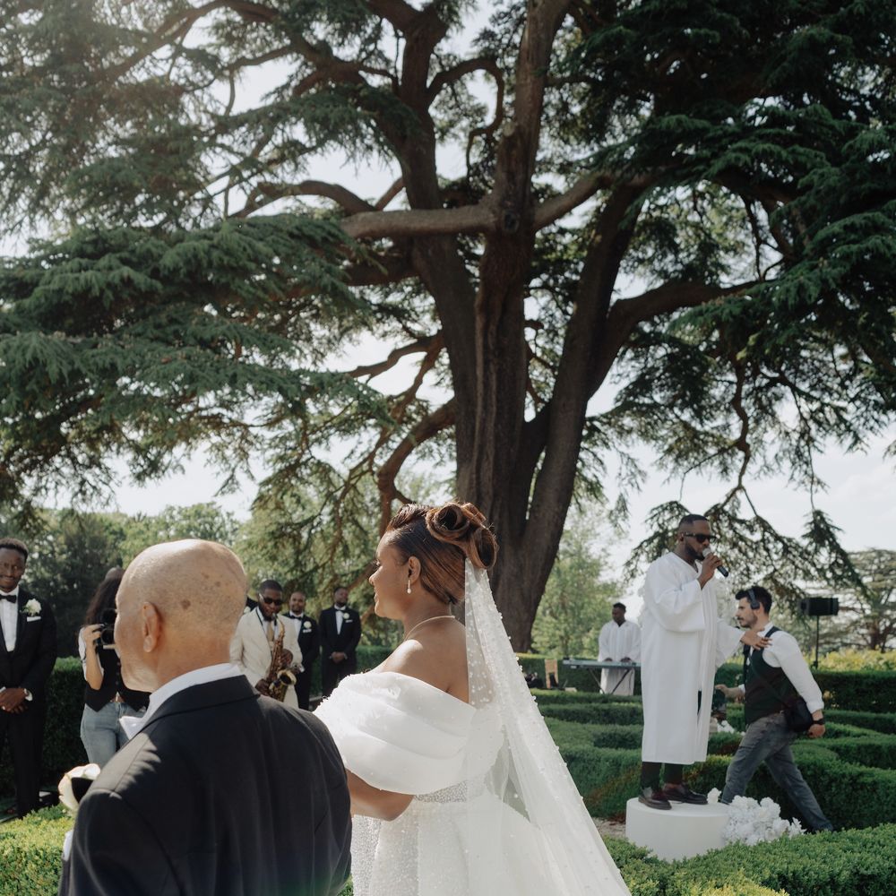 Bride in an off-shoulder sequinned gown and long veil walking down a garden aisle with an escort