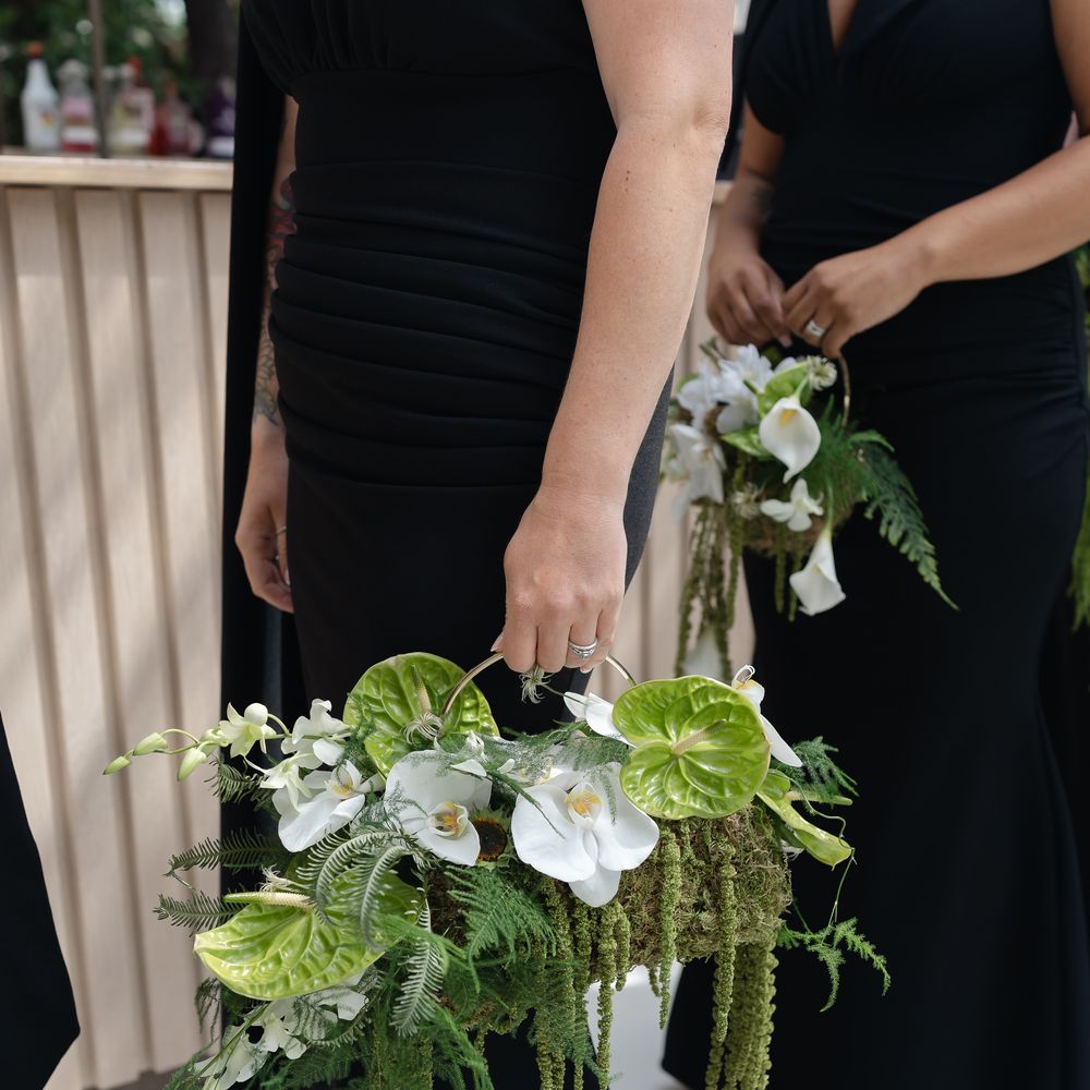 Bridesmaids in black gowns holding trailing green and white orchid and anthurium bouquets