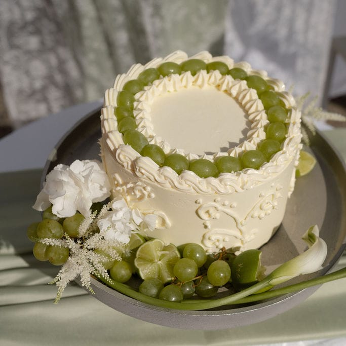 Buttercream wedding cake topped with green grapes, styled with limes, calla lilies and sage linen