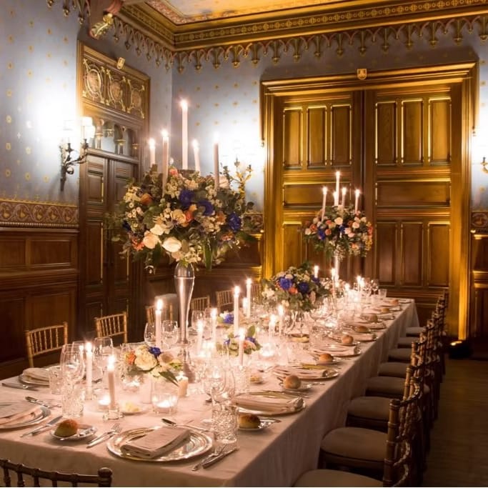 Candlelit banquet table with tall floral arrangements in a panelled stately dining room