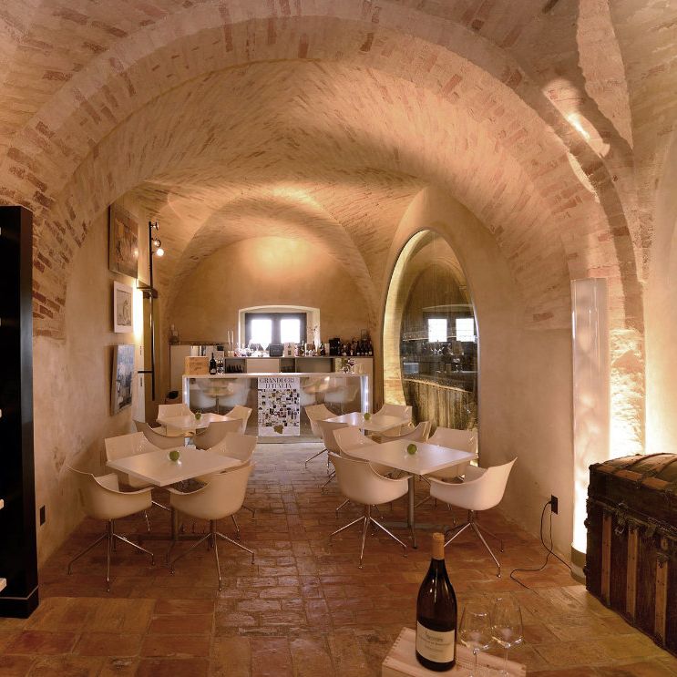 Vaulted brick wine cellar with white modern tables, chairs and shelves of bottles