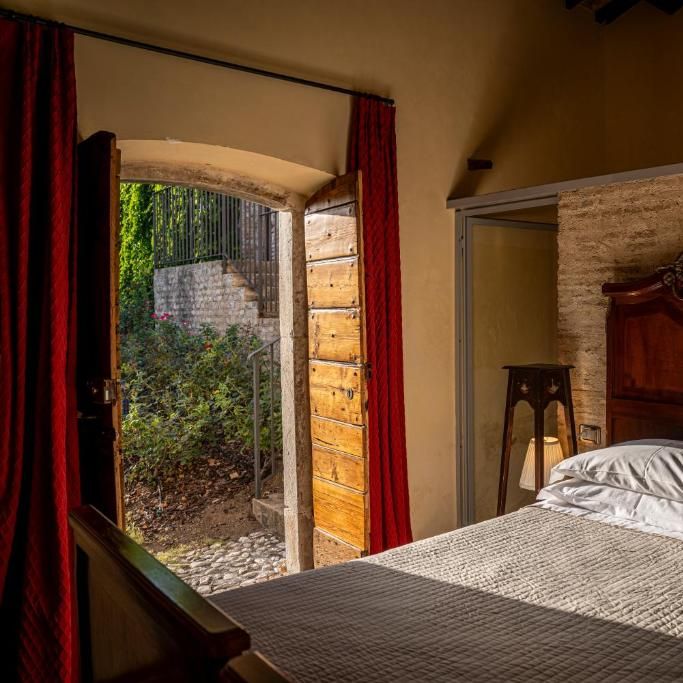 Rustic bedroom with carved wooden headboard and open door leading to a stone courtyard garden