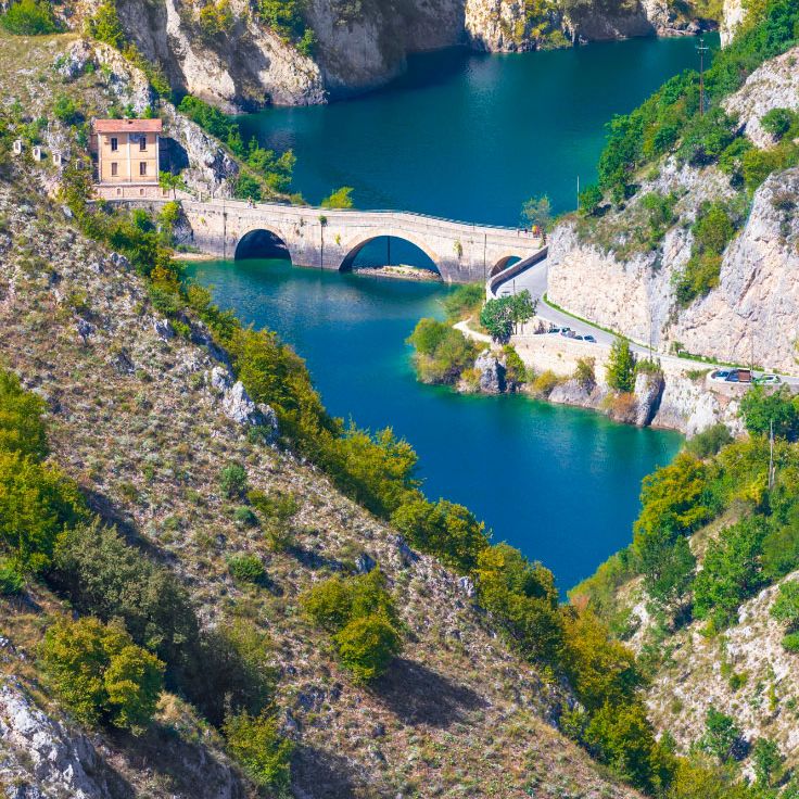 Stone arched bridge crossing a turquoise mountain lake between forested rocky slopes