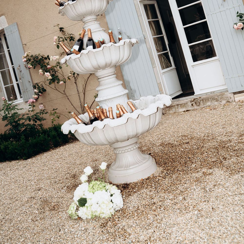 Tiered stone fountain filled with champagne bottles outside a French chateau with blue shutters
