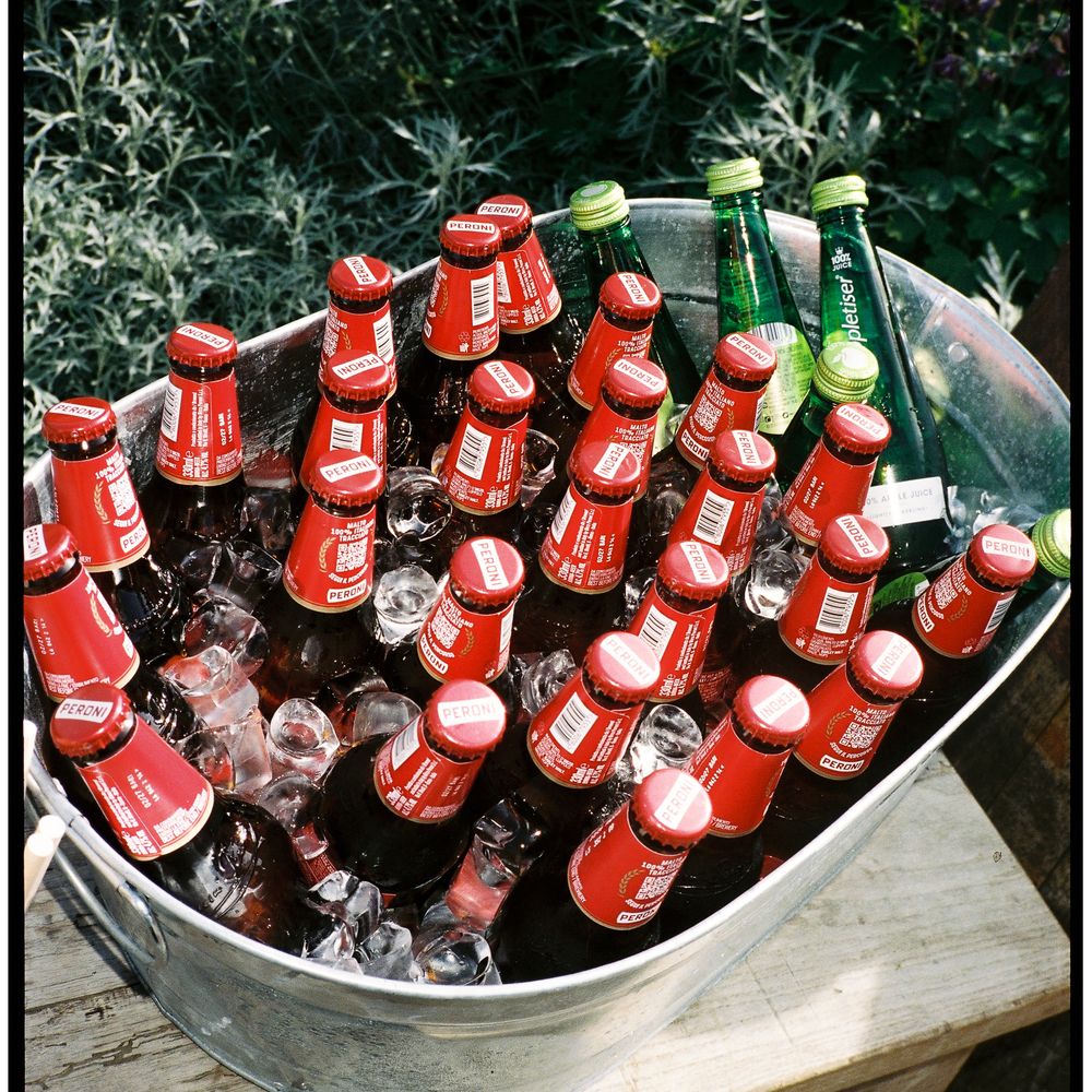 Bottles of beer and elderflower drinks chilling on ice in a metal tub outdoors