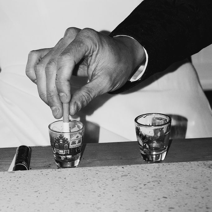 Hand stubbing out a cigarette in a patterned glass beside a lighter on a bar top